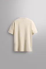 Camiseta color crema de corte relaxed fit, cuello redondo y manga corta. Tiene un texto estampado en el frente y un logo estampado en el ruedo.