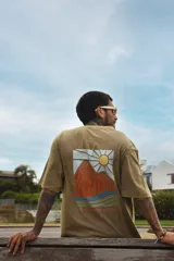 Remera color beige de manga corta con cuello redondo y estampado de un sol con montañas en el pecho.