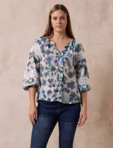 Blusa estampada con flores azules y verdes, cuello a la base con escote en V y volados. Manga larga con puño y apliques de puntilla.