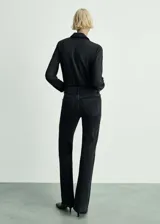 Pantalón de jean negro de tiro medio, corte flare y bajo deshilachado.