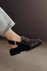 Zueco negro con textura croco, diseño tipo mocasín y tira regulable al talón.