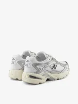 Zapatillas New Balance modelo 725, color blanco con detalles plateados y logo "N" en negro. Diseño inspirado en el estilo de carrera de los años 2000, con malla transpirable, entresuela con amortiguación y suela con agarre.
