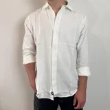 Camisa blanca de lino con corte regular, cuello clásico y mangas largas con puños abotonados.