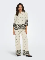 Camisa color crema con estampado de hojas y flores negras, cuello camisero, mangas 3/4 amplias y cierre frontal con botones.