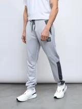 Pantalón de jogging gris claro con recortes laterales en gris oscuro, logo de Umbro estampado en el muslo y cintura ajustable con cordón. Confeccionado en tejido french terry de poliéster.
