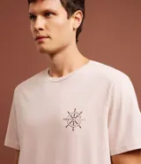 Remera de algodón color rosa claro, de corte clásico, con cuello redondo y manga corta. Presenta un pequeño estampado de un timón en el pecho y un estampado con letras en la espalda.