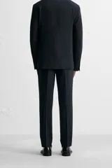 Pantalón de vestir azul marino, de corte slim fit, con bolsillos laterales y traseros. Se ajusta a la cintura con cinturón de cuero marrón.