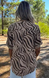 Blusa de algodón con estampado animal print de cebra en tonos camel y marrón oscuro. Posee cuello en V con abertura y un pequeño bolsillo superior. Las mangas son cortas y se pueden doblar.