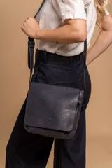 Bandolera de hombro color gris claro, con solapa frontal y correa ajustable. Presenta un diseño simple y práctico, ideal para uso diario.