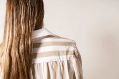 Camisa a rayas verticales color beige y blanco, de corte holgado, con cuello camisero y mangas largas abullonadas con puños abotonados.