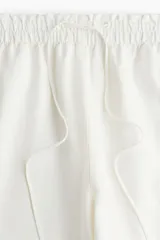 Pantalón de corte holgado color crudo, confeccionado en tejido liviano de mezcla de lino. Modelo de tiro alto con elástico revestido en la cintura, cordón para ajustar y piernas amplias con bolsillos al bies.