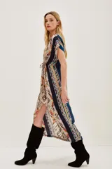 Vestido midi estampado con cuello en V y mangas cortas. Presenta un diseño con cordón ajustable a la cintura y abertura frontal en la falda. El estampado es de estilo étnico o tribal en tonos beige, negro, amarillo y rojo.