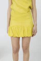 Minifalda amarilla de lino con cintura alta y detalle de volados fruncidos en el ruedo.