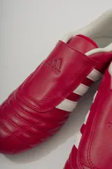 Championes Adidas rojos de cuero sintético, diseñados para taekwondo. Presentan el logo de Adidas en la lengüeta y las tres rayas blancas características en los laterales. El interior es acolchado y de color blanco.