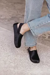 Zuecos negros de cuero con textura de pelo, diseño cerrado con hebilla lateral y tira ajustable en el talón.