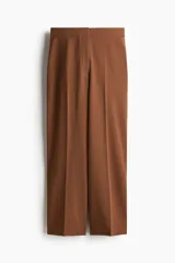 Pantalón tobillero color marrón, de punto pesado, tiro alto, con pliegues delanteros y traseros, elástico en la parte posterior de la pretina, cierre con botón y corchete ocultos, y bajos levemente acampanados.