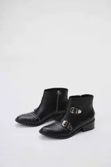 Botas cortas de cuero negro con tachas plateadas en la puntera y el talón, cierre lateral con cremallera y hebillas decorativas. Taco cuadrado bajo.