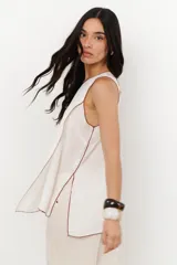 Musculosa color crudo con cuello redondo y ribete marrón en cuello, sisas y ruedo. Diseño cruzado en el frente y aberturas laterales.