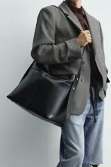 Bolso tipo shopper color negro, con asa de hombro y compartimento principal con cierre de cremallera. El interior cuenta con un bolsillo plano y un bolsillo con cierre de cremallera.
