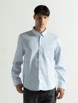 Camisa celeste y blanca a rayas verticales, de manga larga y corte clásico. Tiene cuello abotonado y bolsillo en el pecho.