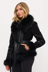 Campera negra de cuero con cuello, puños y ruedo de piel sintética. Tiene cierre frontal asimétrico, cinturón ajustable en la cintura y detalles de tiras de cuero en las mangas.