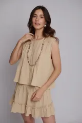 Blusa color beige confeccionada en muselina 100% algodón, con alforzas delanteras y en la espalda, y bordados dorados en las sisas.