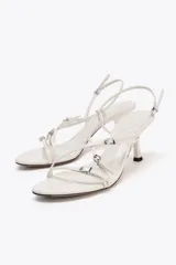 Sandalia de tacón color blanco con tiras finas cruzadas y detalles de hebillas metálicas.