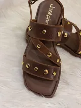 Sandalias bajas de cuero marrón con tiras cruzadas y apliques de tachas doradas.