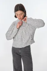 Cardigan color crudo de tejido de punto con diseño trenzado, cuello alto y cierre frontal con cremallera.