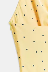 Vestido corto amarillo con lunares negros, escote fluido y tirantes finos con aplicación metálica en la espalda.