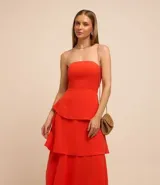Vestido largo sin breteles, color naranja, hecho en crepé. Tiene lastex en la espalda y capas superpuestas en la pollera.