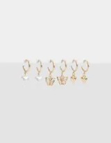 Set de tres pares de aros argolla dorados con dijes colgantes: corazón con perla, mariposa calada y corazón liso.