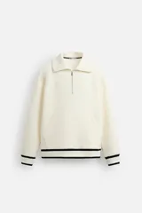 Sudadera color crudo de tejido técnico con cuello alto y cierre de cremallera. Tiene manga larga, corte relaxed fit, bolsillo tipo canguro y rib en puños y bajo con rayas negras.