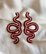 Par de aros colgantes con forma de serpiente dorada contorneada con strass. Cierre a presión de acero inoxidable.