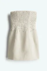 Vestido corto strapless color beige, confeccionado en mezcla de lino y viscosa, con bordado de nudo francés tono sobre tono en la parte superior.