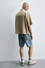 Bermuda de denim de algodón, color gris lavado, con corte relaxed fit y roturas visibles en la parte delantera de ambas piernas. Presenta cinco bolsillos y cierre frontal con cremallera y botón.