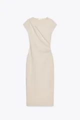 Vestido midi color beige confeccionado en hilatura con algodón. Tiene cuello redondo, manga corta caída y detalle de drapeado lateral.