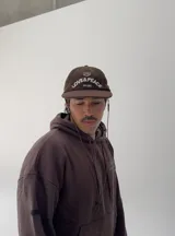 Gorro tipo gorra de béisbol color marrón, confeccionado en pana, con visera corta y bordado frontal en blanco que dice "LOVE & PEACE" y "PP:ONE".