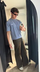 Remera celeste con estampado frontal en blanco, corte boxy y cuello redondo. Pantalón marrón de corte ancho y zapatillas deportivas blancas.