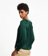 Blusa verde esmeralda de tela satinada, con escote en V, mangas largas con puños abotonados y espalda fruncida.