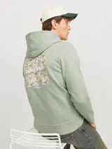 Buzo con capucha verde claro, de corte clásico, con puños y ruedo acanalados. Estampa trasera con diseño abstracto en tonos beige y texto con el logo de la marca.