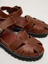 Sandalias romanas de cuero color tostado, con suela de goma y hebilla metálica lateral.