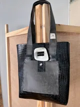 Bolso tote negro con textura símil cuero de cocodrilo, con bolsillo externo decorativo y cierre con botón metálico.