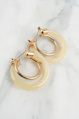 Aros tipo argolla con doble aro, uno de metal dorado y otro de resina color crema.