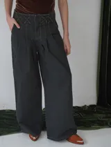 Pantalón vaquero de tiro alto, color gris oscuro, con corte amplio y pinzas en la cintura. Presenta detalle de cruces en la pretina.