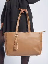 Cartera tote color marrón claro, con doble asa de hombro, cierre superior y doble compartimento interno. Incluye un dije decorativo con forma de borla.