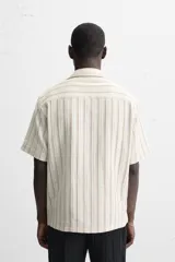 Camisa de manga corta con cuello bowling y corte relaxed fit, confeccionada en tejido con algodón y diseño a rayas verticales en tonos beige y blanco.