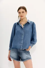 Camisa celeste de tencel con calce recto, manga larga amplia con frunces en los hombros y cuello camisero. Mangas terminadas en puño con botón y ojal. Cartera delantera con botones metálicos con el logo de la marca.