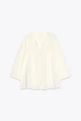 Blusa color crema de cuello redondo con escote pico y manga ancha por debajo del codo. Detalle de acabados con bordados. Cierre frontal con botones.