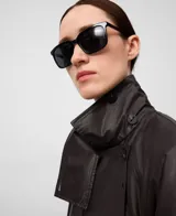 Gabardina larga de mujer, color marrón oscuro, con efecto encerado. Presenta un diseño cruzado con cuello solapa, cierre frontal con botones, cinturón a juego y bolsillos laterales.